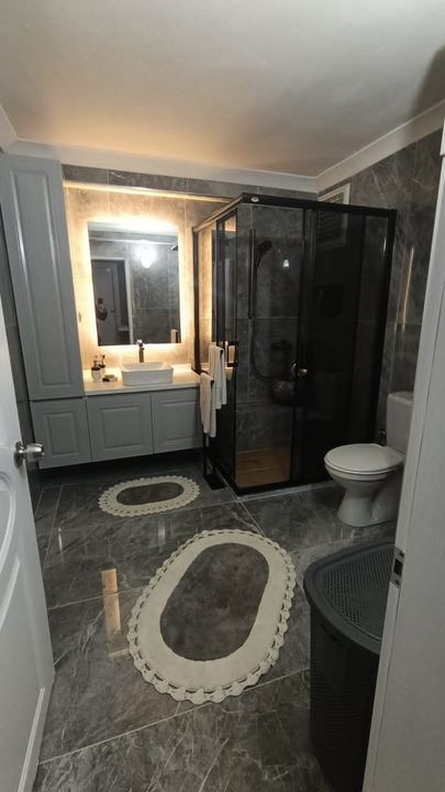 Gri mermer görünümlü banyo, beyaz lavabo dolabı ve siyah çerçeveli duşakabin