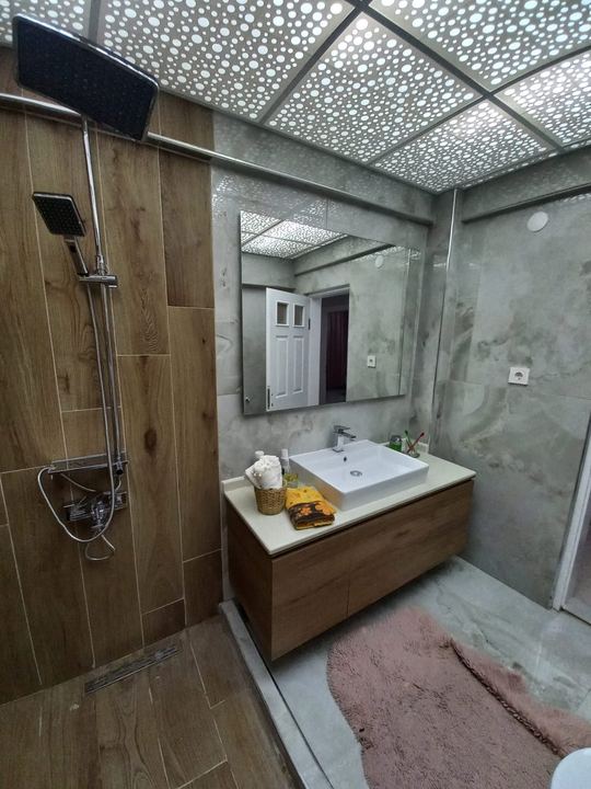 Tepe duşlu duş alanı, ahşap görünümlü fayans ve beyaz lavabo